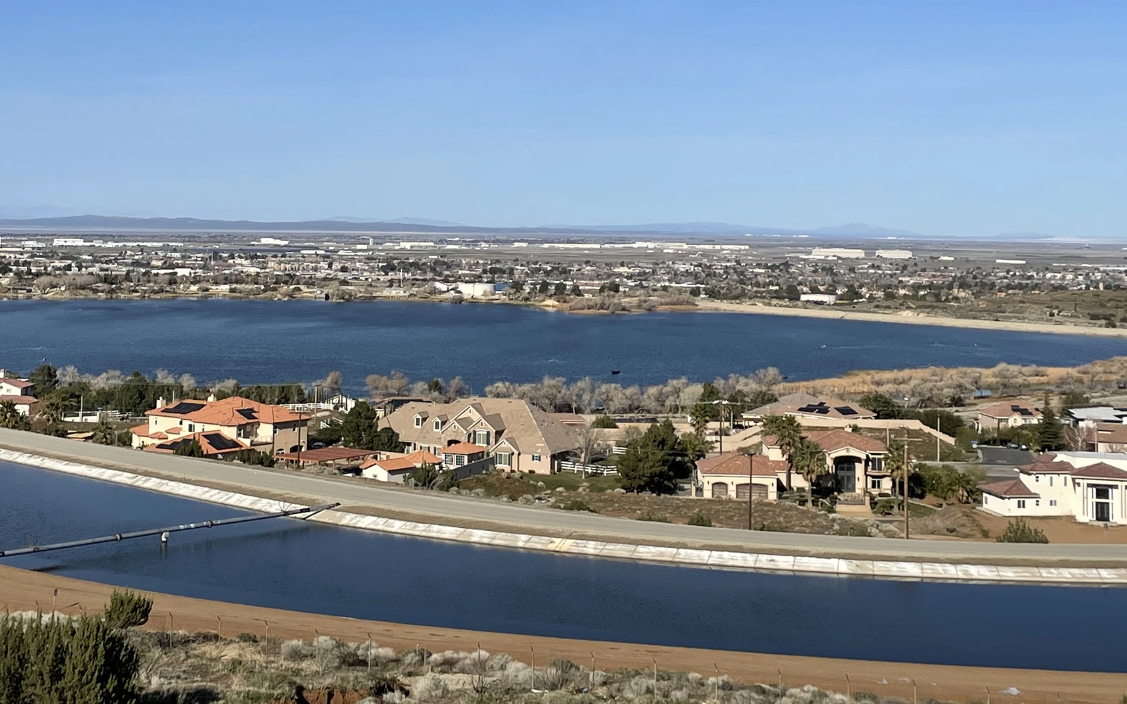 Palmdale and the Antelope Valley floor seen from the Lamont Odett Vista Point, with a lined water channel, houses, a reservoir and distant ranges